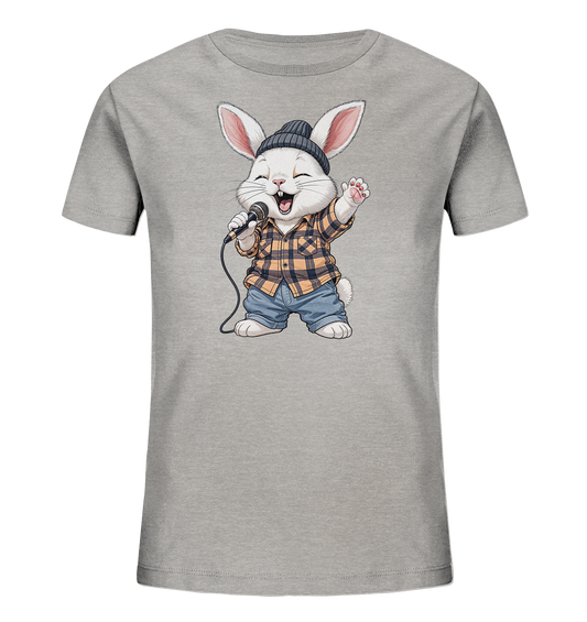 Onlineshop Shirts fuer Kinder - Das Bild zeigt ein hellgraues Kinder-T-Shirt mit einem niedlichen Comic-Hasenmotiv auf der Vorderseite. Der Hase traegt eine dunkle Muetze, ein gelb-schwarz kariertes Hemd und blaue Jeans. Er haelt ein Mikrofon und scheint froehlich zu singen, mit einem geoeffneten Mund und einer erhobenen Pfote. Das Design wirkt verspielt und lebendig, ideal fuer Kinder.
