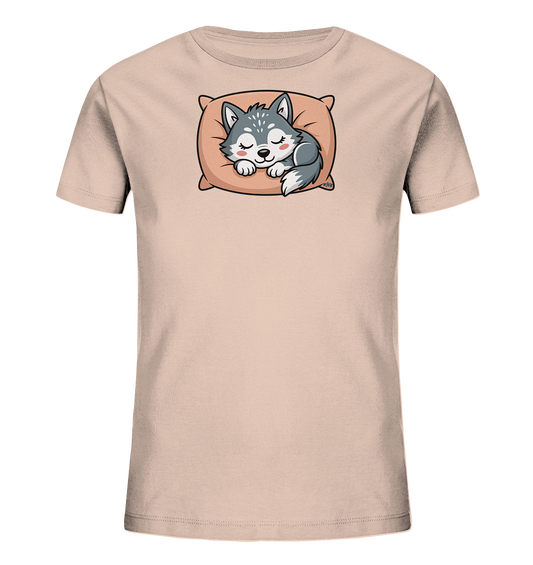Onlineshop Shirts fuer Kinder - Das Bild zeigt ein hellrosafarbenes Kinder-T-Shirt. Auf der Vorderseite ist eine suesse, schlafende Wolfsfigur abgebildet, die auf einem orangefarbenen Kissen liegt. Der Wolf ist in Grautoenen gehalten und hat geschlossene Augen sowie rosige Wangen, was einen friedlichen Ausdruck vermittelt. Das Motiv verleiht dem Shirt eine sanfte und ansprechende Optik.