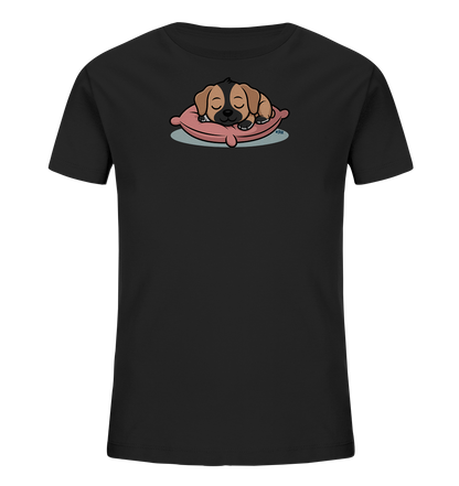 Onlineshop Shirts fuer Kinder - Das Bild zeigt ein schwarzes Kinder-T-Shirt mit einer niedlichen, cartoonhaften Illustration eines schlafenden Welpen. Der Welpe liegt gemuetlich auf einem rosafarbenen Kissen, mit geschlossenen Augen und einem zufriedenen Ausdruck. Das Fell des Welpen ist braun-schwarz gefaerbt, und seine kleinen Pfoten sind unter dem Kopf versteckt. Das Design wirkt sanft und beruhigend, ideal fuer junge Traeger.
