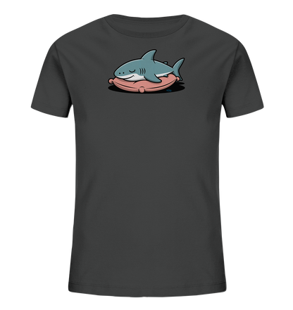 Onlineshop Shirts fuer Kinder - Das Bild zeigt ein dunkelgraues Kinder-T-Shirt mit einem niedlichen Motiv eines schlafenden Hais. Der hellblaue Hai liegt friedlich auf einem rosafarbenen Kissen. Das Design wirkt ruhig und freundlich, ideal fuer Kinder. Es ist eine verspielte Darstellung, die Ruhe ausstrahlt.