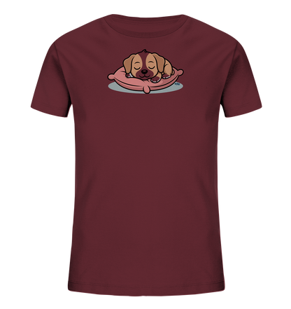 Onlineshop Shirts fuer Kinder - Das Bild zeigt ein dunkelrotes Kinder-T-Shirt mit einem zentral platzierten Motiv. Darauf ist ein schlafender, brauner Welpe zu sehen, der gemuetlich auf einem rosa Kissen liegt. Der Welpe hat geschlossene Augen und wirkt friedlich. Das Design ist niedlich und spricht besonders Kinder an.