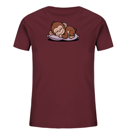 Onlineshop Shirts fuer Kinder - Das Bild zeigt ein dunkelrotes Kinder-T-Shirt, auf dem ein niedliches Äffchen schlafend auf einem hellvioletten Kissen abgebildet ist. Das cartoonhafte Äffchen hat geschlossene Augen und liegt friedlich da. Die Illustration ist detailliert und vermittelt einen ruhigen, liebevollen Ausdruck. Das Design ist schlicht und auf die Mitte des Shirts fokussiert.