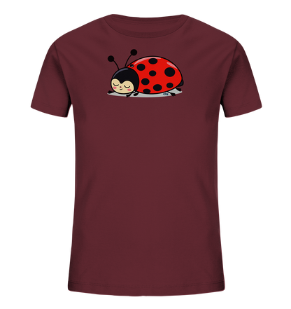 Onlineshop Shirts fuer Kinder - Das Bild zeigt ein dunkelrotes Kinder-T-Shirt mit einem niedlichen Marienkaefer-Motiv auf der Vorderseite. Der Marienkaefer ist rot mit schwarzen Punkten und hat geschlossene Augen, was einen schlafenden oder zufriedenen Ausdruck vermittelt. Er liegt auf einem hellgrauen Untergrund, der als Schatten dient. Das Design wirkt verspielt und liebevoll.
