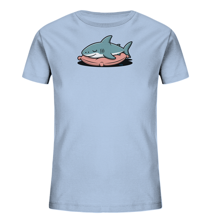 Onlineshop Shirts fuer Kinder - Das Bild zeigt ein hellblaues Kinder-T-Shirt. Auf der Vorderseite ist ein schlafender, freundlicher Cartoon-Hai abgebildet. Der Hai liegt gemuetlich auf einem rosa Kissen, was dem Design eine ruhige und niedliche Note verleiht. Die Gestaltung ist verspielt und ansprechend fuer Kinder.