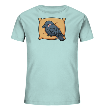 Onlineshop Shirts fuer Kinder - Das Bild zeigt ein hellblaues Kinder-T-Shirt mit einem niedlichen Motiv in der Mitte. Darauf ist ein dunkelgrauer Rabe abgebildet, der friedlich auf einem beigen Kissen schlaeft. Die Illustration wirkt gemuetlich und entspannt, mit sanften Farbtoenen, die gut zum Untergrund passen. Das Design verleiht dem Shirt einen verspielten und beruhigenden Charakter.