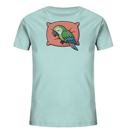 Onlineshop Shirts fuer Kinder - Das Bild zeigt ein hellblaues Kinder-T-Shirt. Auf der Vorderseite ist ein schlafender, gruener Papagei mit blauen Fluegeln und Schwanzfedern abgebildet. Der Papagei ruht auf einem roetlich-orangen Kissen und hat die Augen geschlossen. Das Design wirkt friedlich und verspielt.