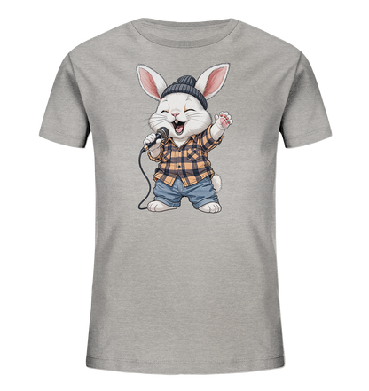 Onlineshop Shirts fuer Kinder - Das Bild zeigt ein hellgraues Kinder-T-Shirt mit einem niedlichen Comic-Hasenmotiv auf der Vorderseite. Der Hase traegt eine dunkle Muetze, ein gelb-schwarz kariertes Hemd und blaue Jeans. Er haelt ein Mikrofon und scheint froehlich zu singen, mit einem geoeffneten Mund und einer erhobenen Pfote. Das Design wirkt verspielt und lebendig, ideal fuer Kinder.
