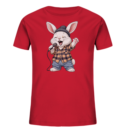 Onlineshop Shirts fuer Kinder - Das Bild zeigt ein rotes T-Shirt fuer Kinder. Auf der Vorderseite ist eine froehliche Comic-Figur eines Hasen abgebildet, der ein kariertes Hemd, Jeans-Shorts und eine Muetze traegt. Der Hase haelt ein Mikrofon und scheint zu singen oder zu rappen, mit einer Pfote in die Luft gestreckt. Das Design wirkt dynamisch und ansprechend.