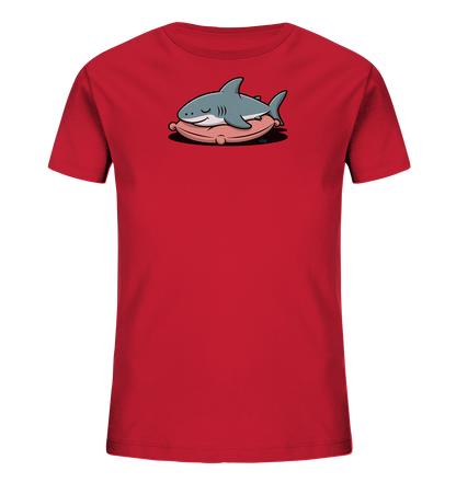 Onlineshop Shirts fuer Kinder - Das Bild zeigt ein rotes Kinder-T-Shirt mit einem niedlichen Aufdruck eines schlafenden Hais. Der graue Cartoon-Hai liegt friedlich auf einem weichen, rosafarbenen Kissen und hat die Augen geschlossen. Das Design wirkt verspielt und laedt zum Traeumen ein. Das T-Shirt ist schlicht gehalten, um den Fokus auf das Hauptmotiv zu legen.