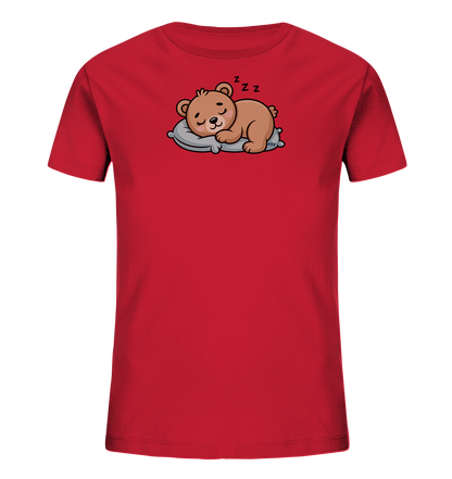 Onlineshop Shirts fuer Kinder - Das Bild zeigt ein rotes T-Shirt fuer Kinder. Auf der Vorderseite ist eine niedliche, cartoonartige Illustration eines schlafenden Baeren zu sehen. Der hellbraune Baer liegt friedlich auf einem grauen Kissen, mit geschlossenen Augen und Zzz-Symbolen ueber seinem Kopf. Das Motiv verleiht dem Shirt einen gemuetlichen und verspielten Charakter.