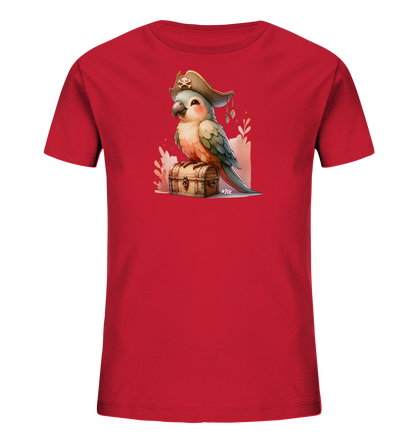 Onlineshop Shirts fuer Kinder - Das Bild zeigt ein rotes Kinder T-Shirt mit einer detaillierten Grafik. Darauf sitzt ein farbenfroher Cartoon-Papagei mit Piratenhut auf einer hoelzernen Schatzkiste. Im Hintergrund sind sanfte, stilisierte Blaetter und Ranken zu sehen. Das gesamte Motiv ist froehlich und kindgerecht gestaltet.