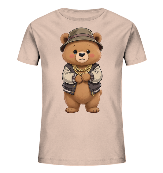 Onlineshop Shirts fuer Kinder - Das Bild zeigt ein hellbeiges Kinder-T-Shirt mit einem niedlichen Baerenmotiv auf der Vorderseite. Der Baer traegt einen olivgruenen Hut, eine braune Bomberjacke mit beigen Ärmeln und eine goldene Kette. Er steht mit verschraenkten Armen da und hat einen freundlichen Ausdruck. Das Design wirkt verspielt und gleichzeitig laessig.
