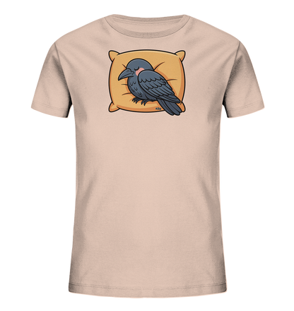 Onlineshop Shirts fuer Kinder - Das Bild zeigt ein helles Kinder-T-Shirt mit einem niedlichen Motiv eines schlafenden Raben. Der Rabe, in dunklem Grau gehalten, ruht gemuetlich auf einem orangefarbenen Kissen, mit geschlossenen Augen und einem rosafarbenen Wangenrouge. Das Design wirkt beruhigend und ist ideal fuer kleine Schlafmuetzen.
