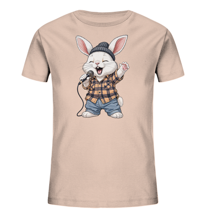Onlineshop Shirts fuer Kinder - Das Bild zeigt ein Kinder-T-Shirt in hellem Beige. Auf der Vorderseite ist ein aufgedruckter Hase zu sehen, der eine dunkle Muetze, ein kariertes Hemd und Jeans traegt. Der Hase haelt ein Mikrofon und singt mit geschlossenen Augen und erhobener Pfote, was einen lebhaften und froehlichen Eindruck vermittelt. Das Motiv verleiht dem Shirt einen verspielten Charakter.