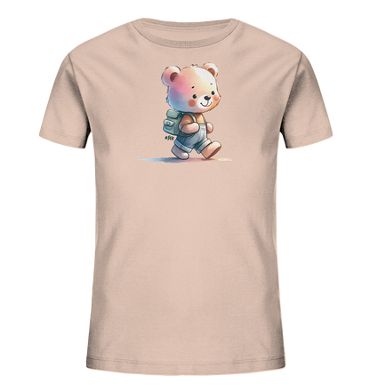 Onlineshop Shirts für Kinder - Das Bild zeigt ein hellrosa T-Shirt für Kinder mit einer niedlichen Comic-Bären-Grafik auf der Vorderseite. Der Bär ist in Overalls und mit einem Rucksack abgebildet, wie er lächelnd geht. Das Design hat einen Aquarell-Stil mit dezenten Farbschattierungen und zarten Farbstreifen darunter. Ein kleines Hashtag-Detail ergänzt die fröhliche Illustration.