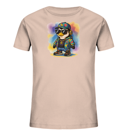 Onlineshop Shirts fuer Kinder - Das hellbeige T-Shirt zeigt einen coolen Cartoon-Pinguin. Der Pinguin traegt Sonnenbrille, Basecap, Kopfhoerer und eine bunte Jacke. Er steht vor einem Hintergrund aus farbigen Aquarell-Flecken, was dem Design eine lebhafte Note verleiht. Das Motiv wirkt modern und verspielt.