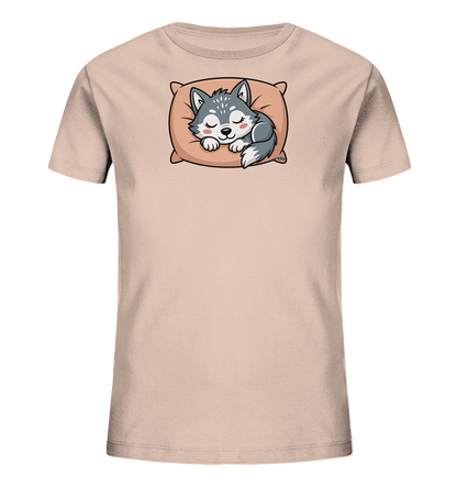 Onlineshop Shirts fuer Kinder - Das Bild zeigt ein hellrosafarbenes Kinder-T-Shirt. Auf der Vorderseite ist eine suesse, schlafende Wolfsfigur abgebildet, die auf einem orangefarbenen Kissen liegt. Der Wolf ist in Grautoenen gehalten und hat geschlossene Augen sowie rosige Wangen, was einen friedlichen Ausdruck vermittelt. Das Motiv verleiht dem Shirt eine sanfte und ansprechende Optik.