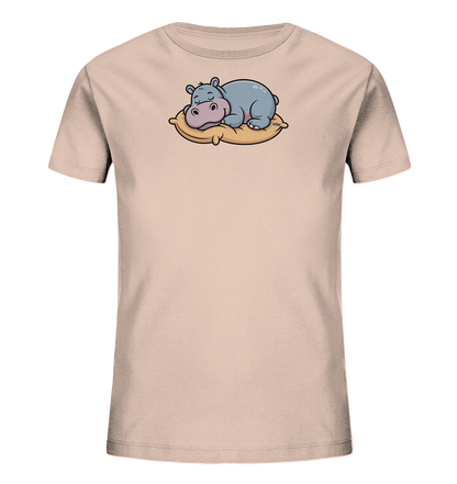 Onlineshop Shirts fuer Kinder - Das Bild zeigt ein hellrosafarbenes Kinder-T-Shirt. Auf der Vorderseite ist eine niedliche Cartoon-Illustration eines schlafenden Nilpferds zu sehen. Das Nilpferd liegt gemuetlich auf einem beigen Kissen. Das Design wirkt ruhig und kindgerecht.