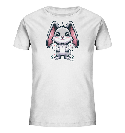 Onlineshop Shirts fuer Kinder - Das Bild zeigt ein weisses T-Shirt fuer Kinder. Auf der Vorderseite ist eine niedliche, grau-weisse Cartoon-Illustration eines Hasen abgebildet. Der Hase hat grosse rosa Ohren, grosse Augen und steht im Gras, umgeben von kleinen Sternen und Glitzerpunkten. Das Design wirkt freundlich und verspielt.