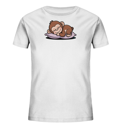 Onlineshop Shirts fuer Kinder - Das Bild zeigt ein weisses Kinder-T-Shirt mit einem niedlichen Motiv auf der Vorderseite. Darauf ist ein kleiner brauner Affe abgebildet, der friedlich auf einem lilafarbenen Kissen schlaeft. Das Äffchen hat geschlossene Augen und ein leichtes Laecheln, was dem Design eine ruhige und liebliche Ausstrahlung verleiht. Die Abbildung ist zentral im oberen Bereich des Shirts platziert.
