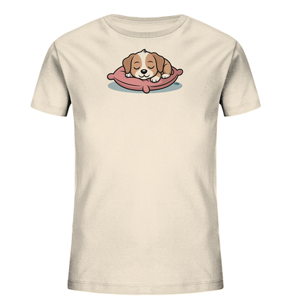Onlineshop Shirts fuer Kinder - Das Bild zeigt ein hellbeiges Kinder-T-Shirt mit einem niedlichen Motiv eines schlafenden Welpen. Der Welpe liegt friedlich auf einem rosa Kissen, die Augen geschlossen. Das Design strahlt Ruhe und Gemuetlichkeit aus und ist ideal fuer kleine Tierliebhaber. Die Farben sind sanft und harmonisch aufeinander abgestimmt.