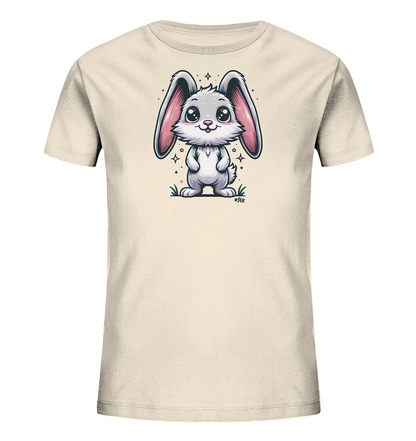 Onlineshop Shirts fuer Kinder - Das Bild zeigt ein beigefarbenes T-Shirt fuer Kinder mit einem niedlichen, cartoonartigen Hasenmotiv auf der Vorderseite. Der Hase hat grosse Ohren, ein freundliches Laecheln und ist von kleinen Sternen umgeben. Er steht auf einer Flaeche, die Gras darstellt. Das Design wirkt verspielt und ansprechend.