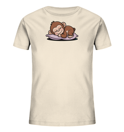 Onlineshop Shirts fuer Kinder - Das Bild zeigt ein hellbeiges T-Shirt fuer Kinder. Auf der Vorderseite ist eine niedliche Cartoon-Illustration eines schlafenden Äffchens zu sehen. Das braune Äffchen liegt friedlich auf einem lilafarbenen Kissen, die Augen geschlossen. Dieses Motiv verleiht dem Shirt einen ruhigen und verspielten Charakter.
