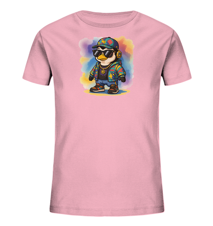Onlineshop Shirts fuer Kinder - Das Bild zeigt ein hellrosa T-Shirt mit einem aufgedruckten, modischen Pinguin. Der Pinguin traegt eine bunte Kappe, Sonnenbrille und Kopfhoerer, ergaenzt durch eine goldene Kette. Er ist in einer farbenfrohen Jacke und Sneakers gekleidet und steht vor einem mehrfarbigen Aquarell-Hintergrund. Dieses Design verleiht dem Shirt einen laessigen und verspielten Charakter.
