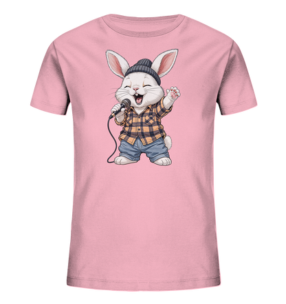 Onlineshop Shirts fuer Kinder - Das Bild zeigt ein rosafarbenes Kinder-T-Shirt mit einem froehlichen Hasenmotiv auf der Vorderseite. Der Hase traegt eine Muetze, ein kariertes Hemd und Jeans und haelt ein Mikrofon, als ob er singen wuerde. Sein Mund ist offen und eine Pfote ist erhoben, was eine lebendige Szene darstellt. Das Design ist verspielt und ansprechend fuer Kinder.
