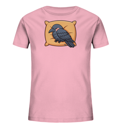 Onlineshop Shirts fuer Kinder - Das Bild zeigt ein hellrosa Kinder-T-Shirt mit einem niedlichen Motiv eines schlafenden Vogels. Ein dunkler Vogel, der einem Raben aehnelt, liegt friedlich auf einem weichen, goldfarbenen Kissen. Der Vogel hat die Augen geschlossen und wirkt sehr entspannt, was eine ruhige Atmosphaere schafft. Das Design ist schlicht und liebevoll gestaltet.